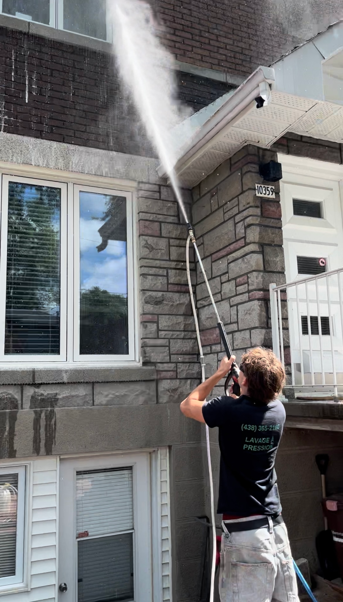 Un homme nettoie un bâtiment en briques avec un nettoyeur haute pression.
