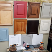 Assorted cabinet door samples in wood, white, red, black, blue, and gray displayed on a wall.