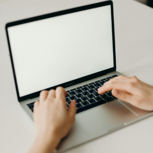 Hands typing on a laptop with a blank white screen in a bright workspace