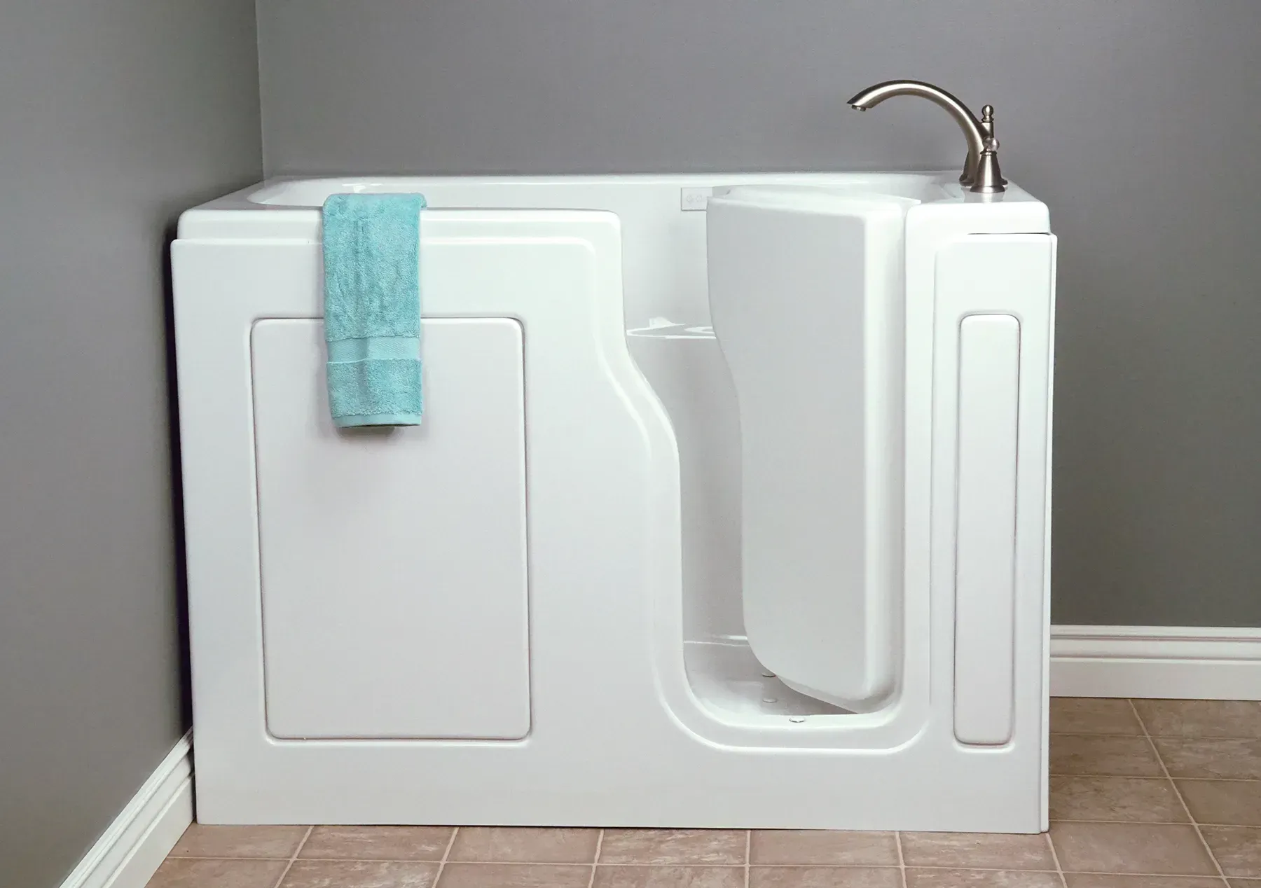 White walk-in bathtub with built-in seat, chrome faucet, and turquoise towel in a bathroom