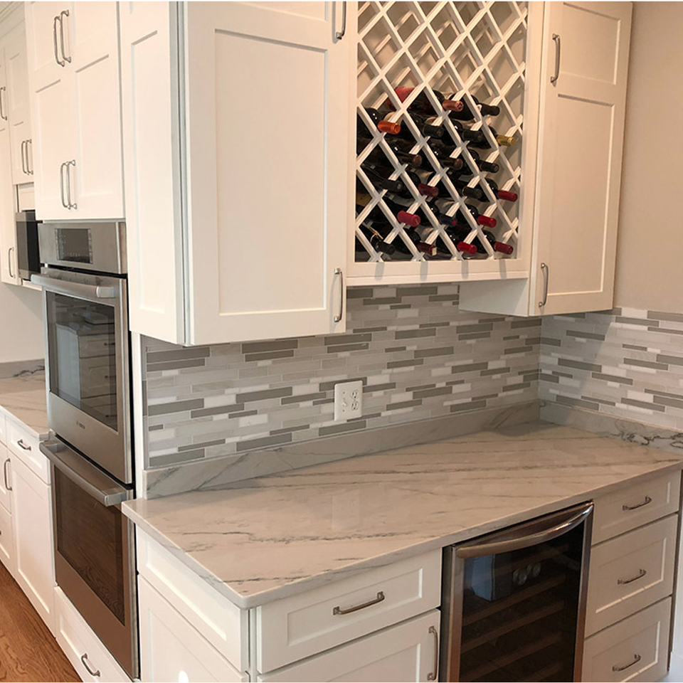 Modern kitchen with white cabinets, gray tile backsplash, built-in oven, and wine rack above the counter