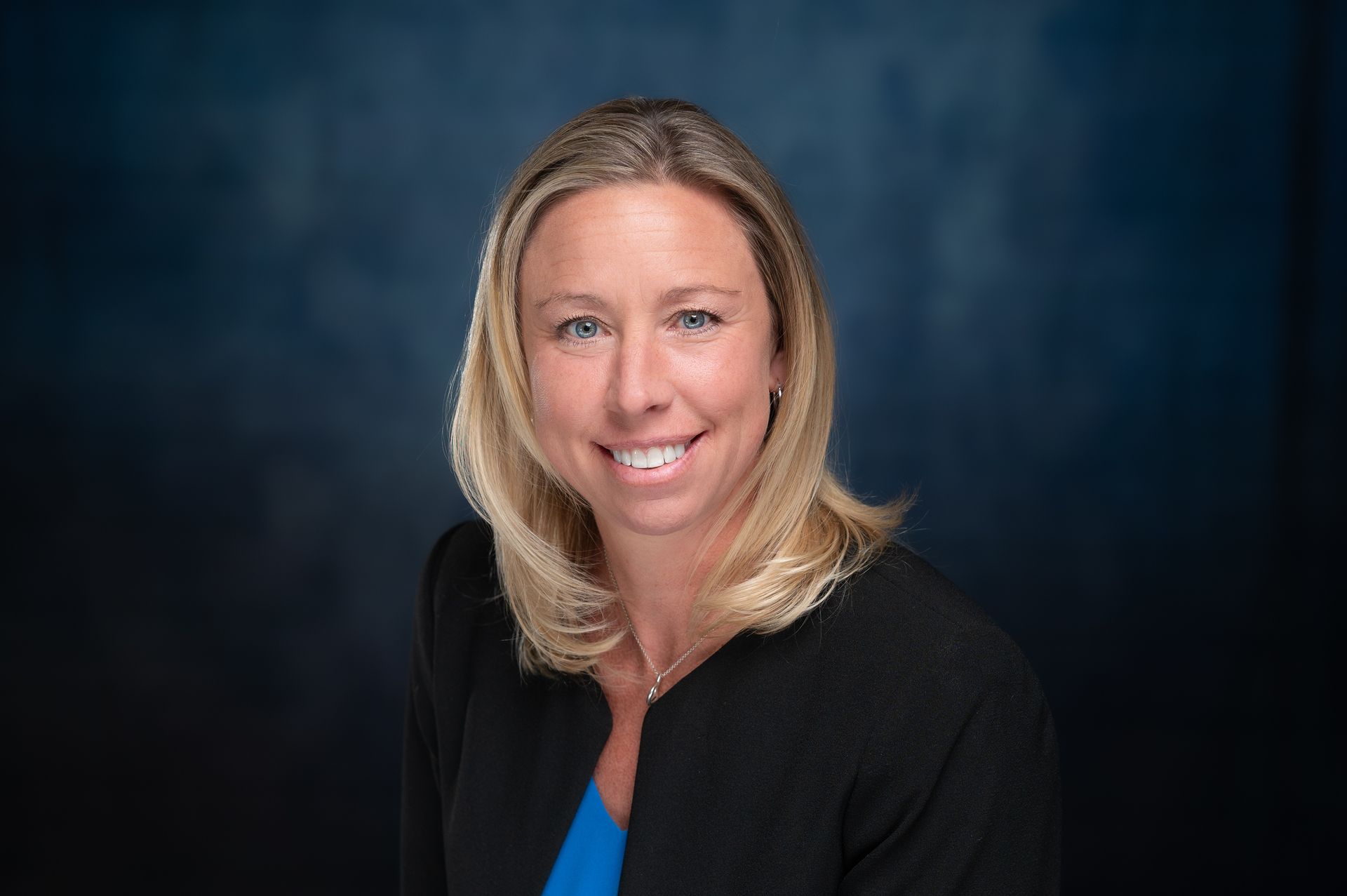 A woman in a black jacket and blue shirt is smiling for the camera.