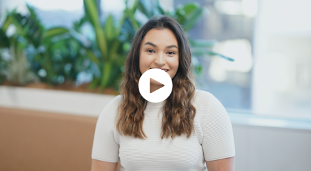 A woman in a white shirt is sitting in front of a window and smiling.
