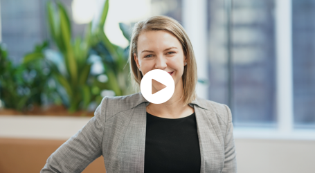 A woman in a suit is smiling in front of a play button.