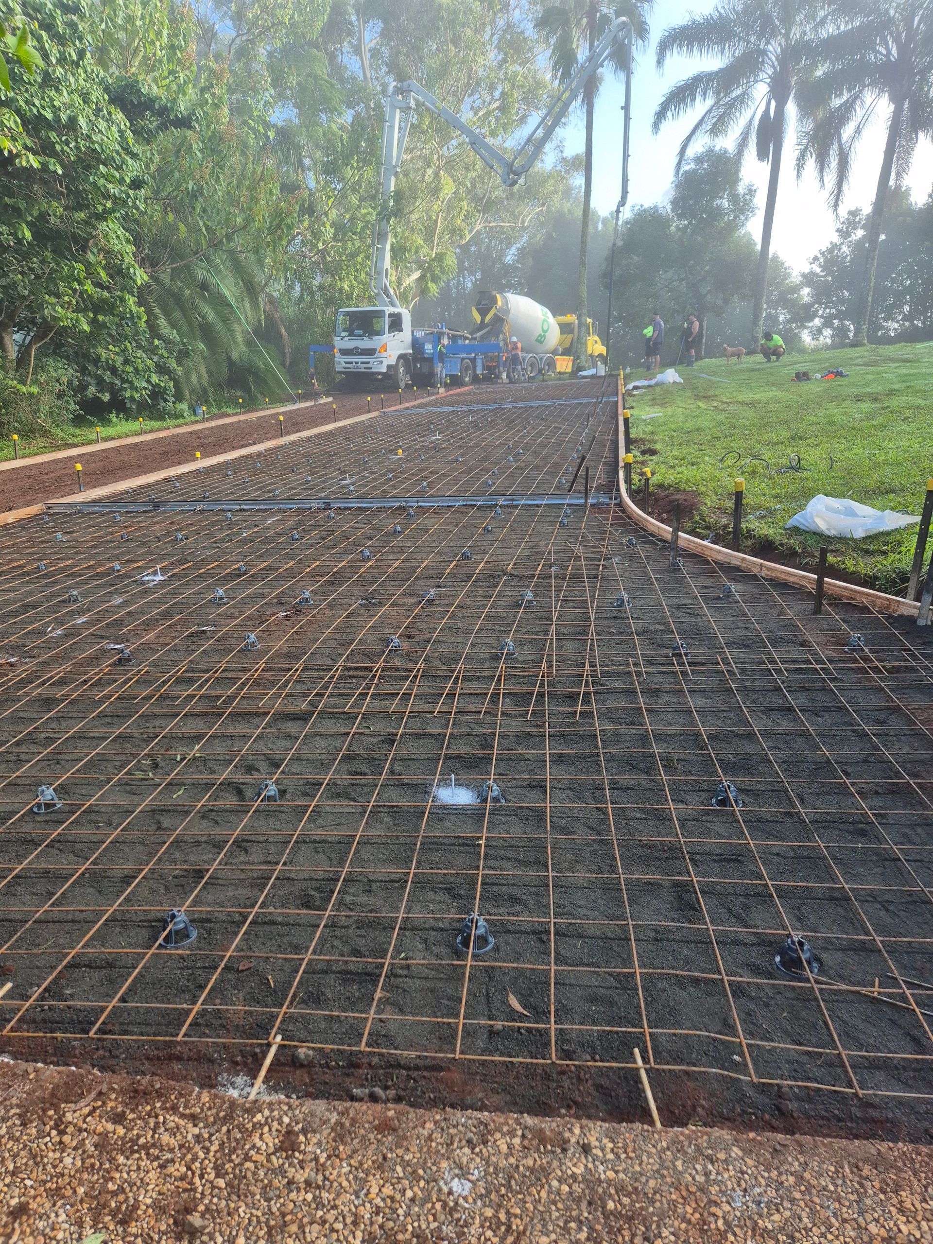 Driveway under construction with rebar grid, concrete truck in the background, green grass and trees— All Around Concreting in Wollongbar, NSW