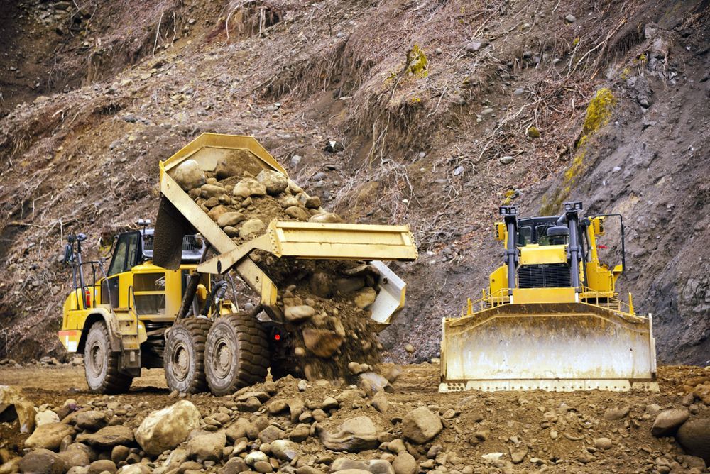Yellow Dump Truck Dumping Rocks With a Bulldozer Beside It in a Construction Site — All Around Concreting in Wollongbar, NSW