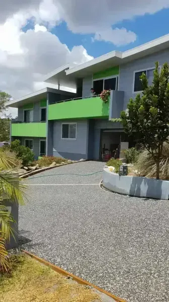 Two-story House With Green Accents and Gray Exterior, Gravel Driveway, and Blue Sky — All Around Concreting in Lismore, NSW