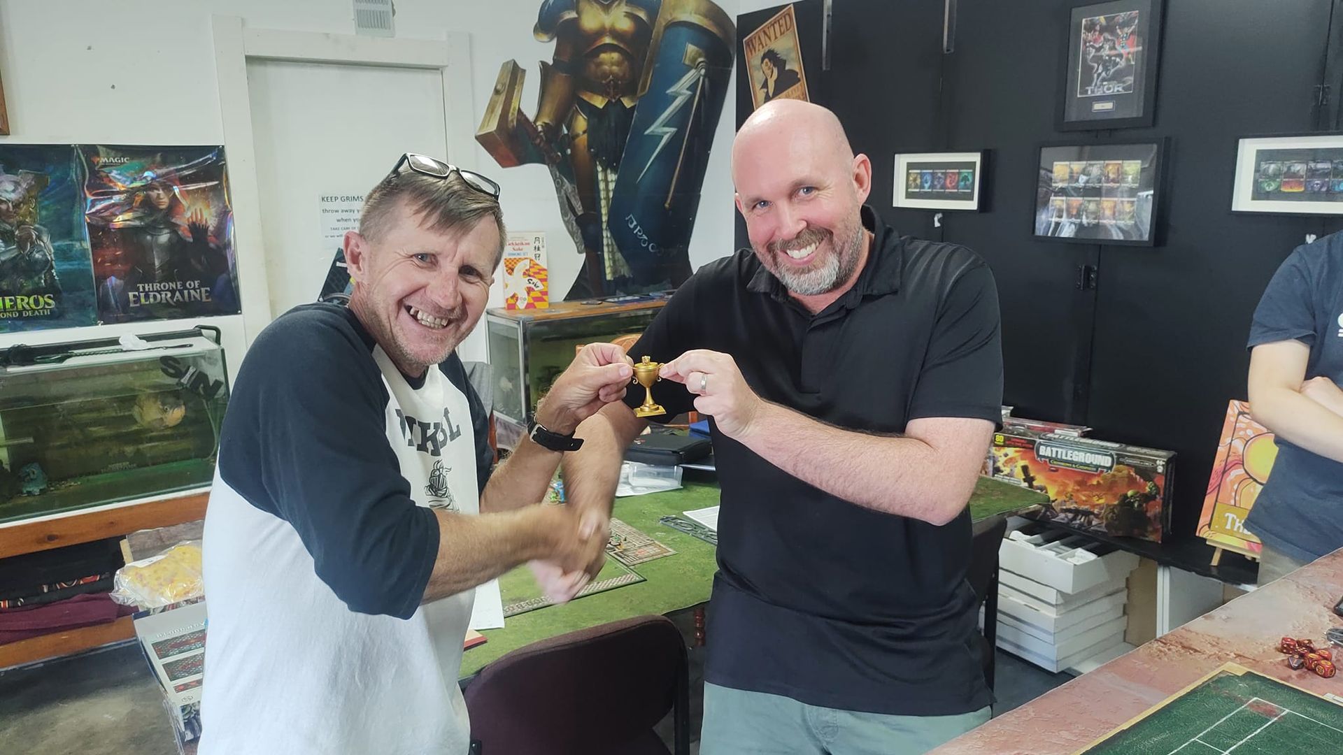 Two Men Smiling, Shaking Hands, Holding a Trophy in a Game Store — Grim Gaming & Hobbies in Bundaberg Central, QLD