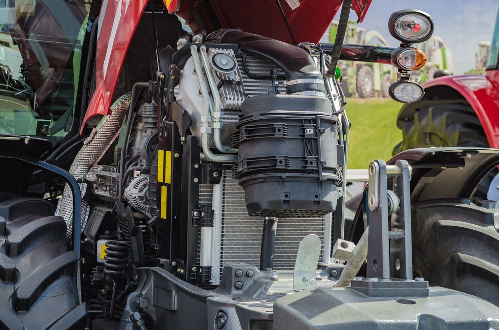 Close-up of a tractor engine with red body panels and large rear wheels in a farm setting — Bundaberg Field Service in Bargara, QLD