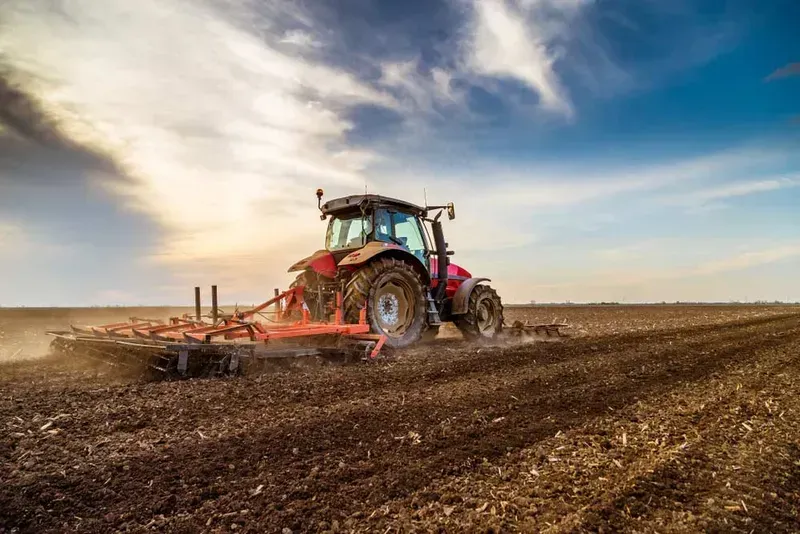 Red tractor plowing a brown field under a dramatic cloudy sky — Bundaberg Field Service in Bargara, QLD