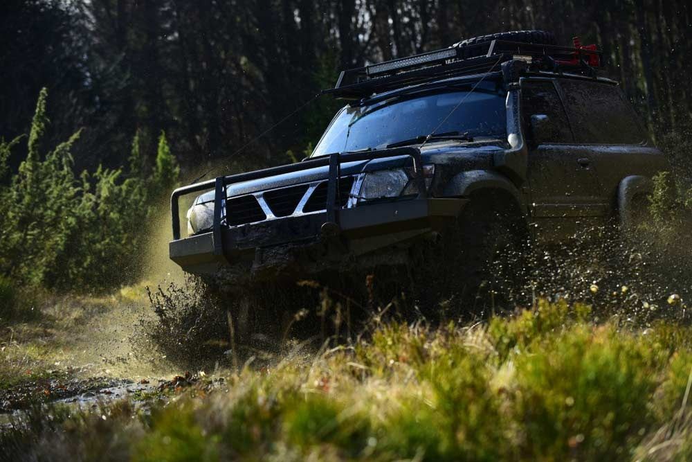 Black off-road SUV driving through a muddy forest trail, kicking up water and dirt — Bundaberg Field Service in Bargara, QLD