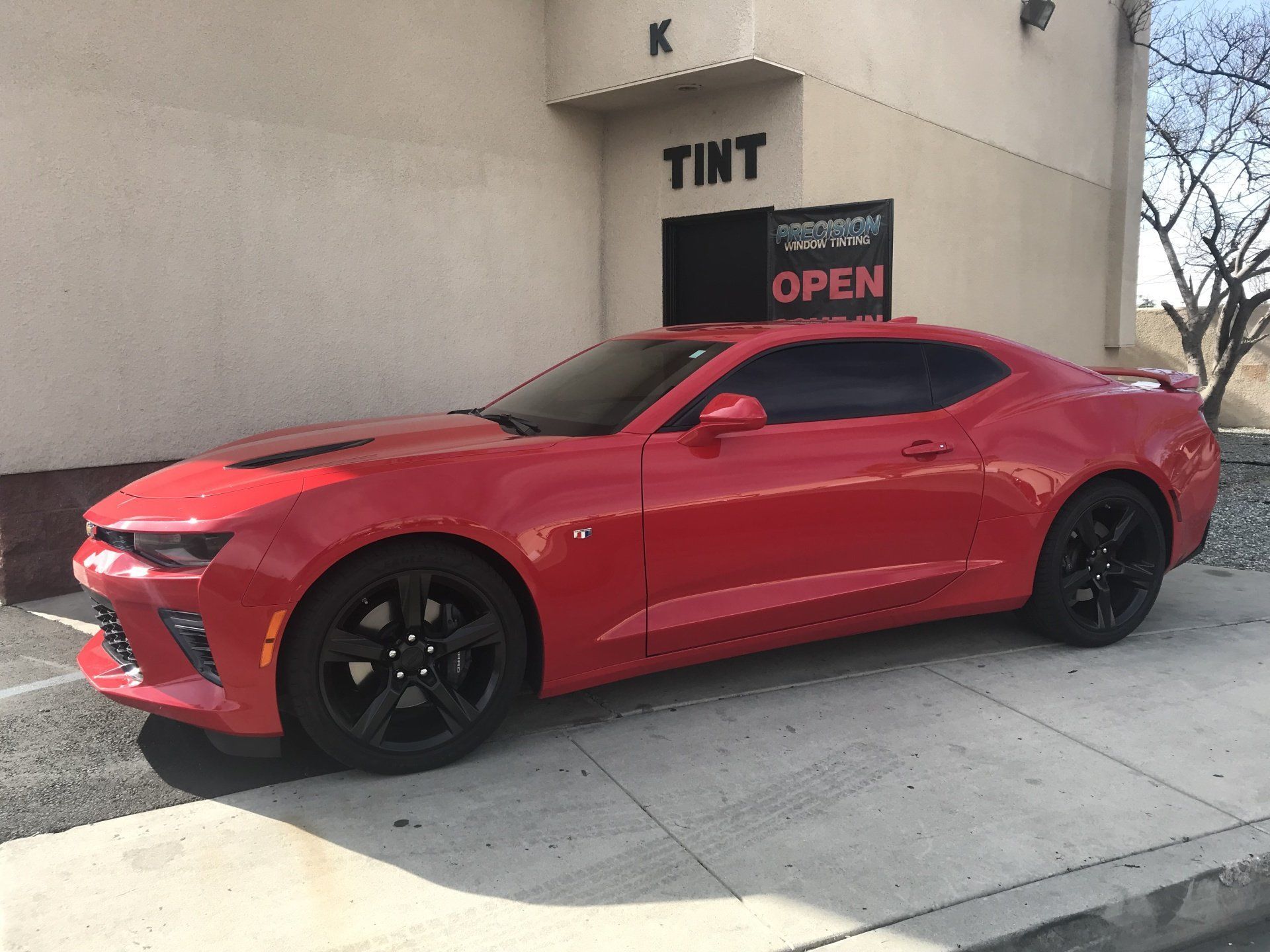 A red car is parked in front of a building that says tint open