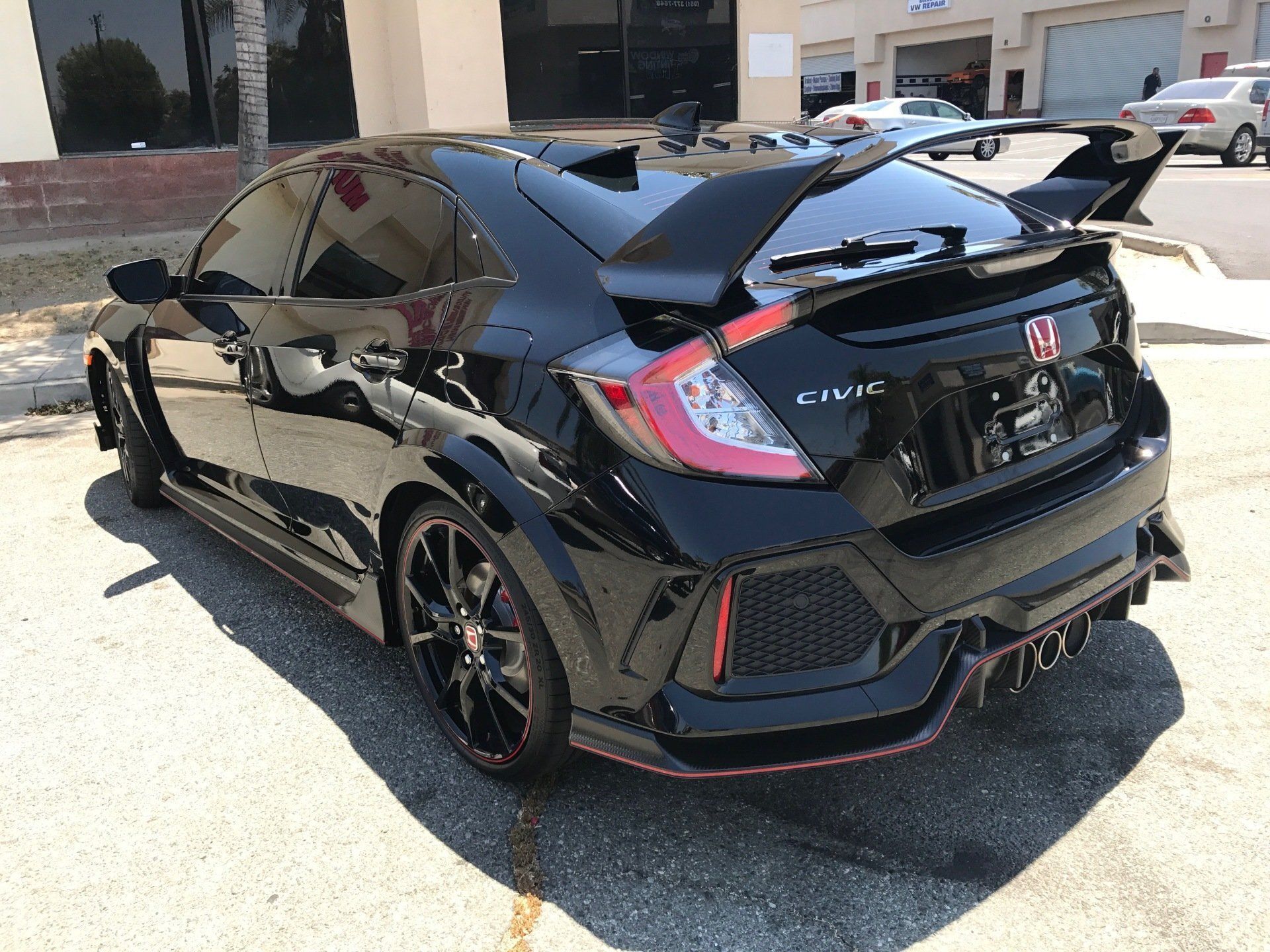 A black Honda Civic type r is parked in front of a building