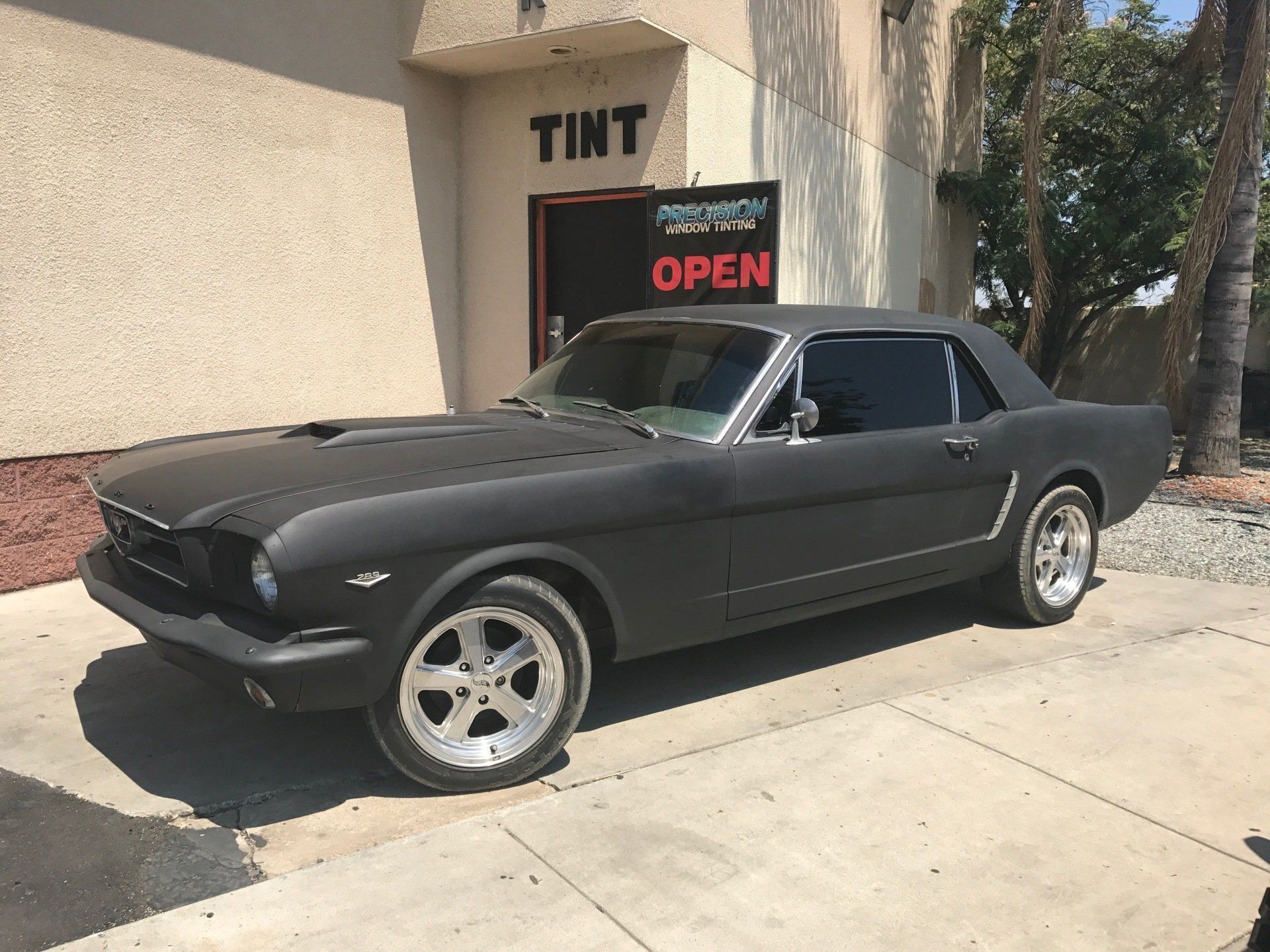 A black Mustang is parked in front of a tint shop