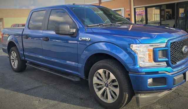 A blue Ford f150 truck is parked in front of a building