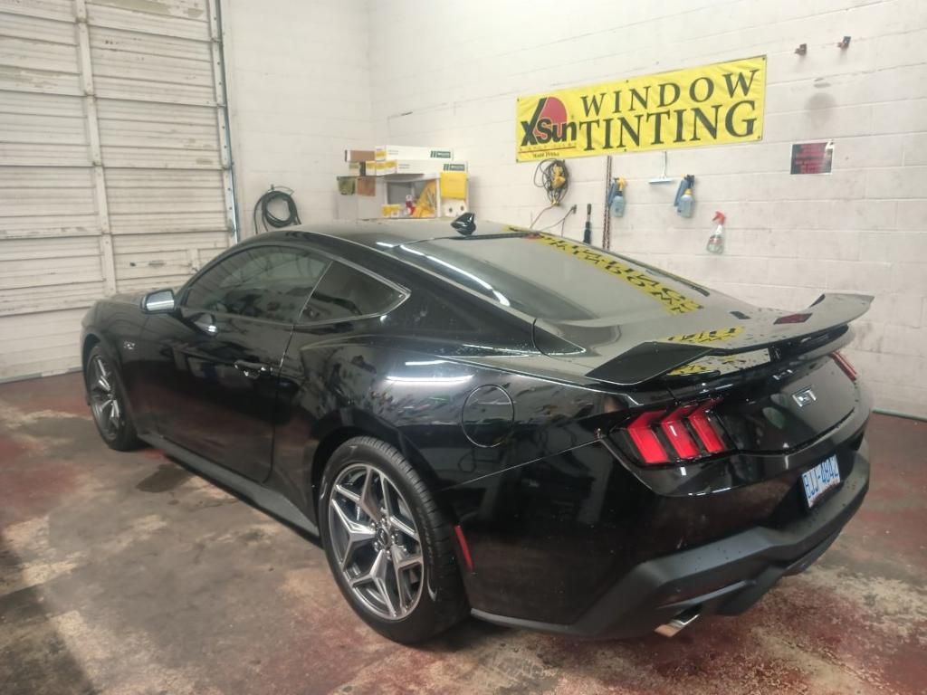 A black ford mustang is parked in a garage next to a window tinting sign.