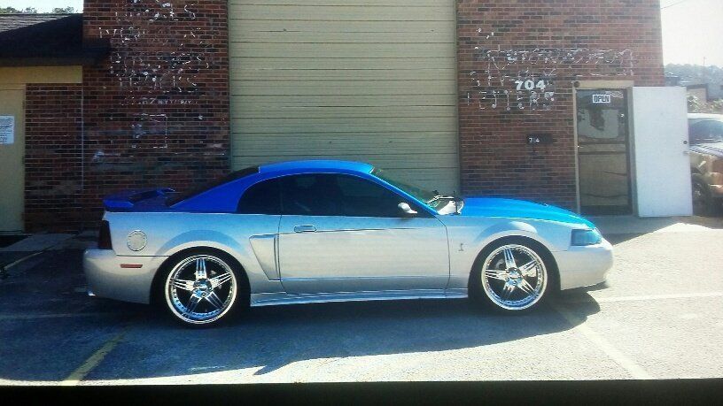 A silver mustang with a blue top is parked in a parking lot