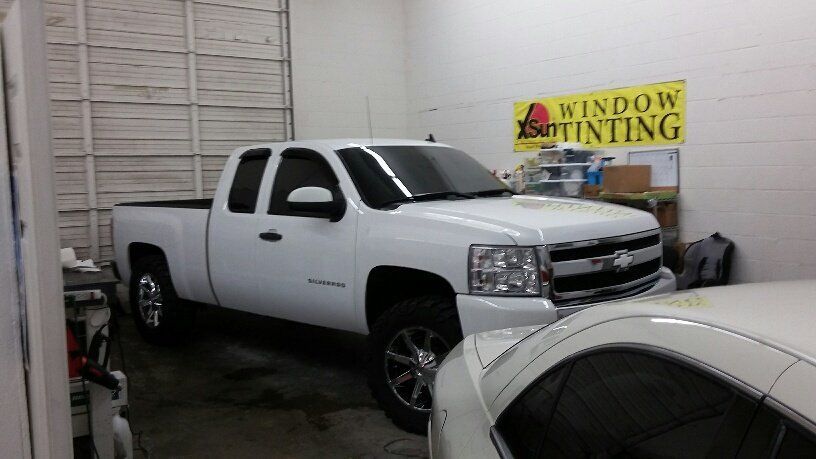 A white truck is parked in a garage next to a sign that says window tinting