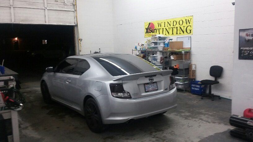 A silver car is parked in front of a window tinting sign