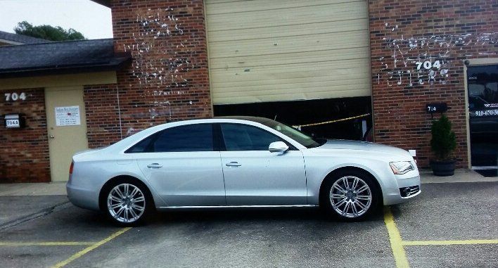 A silver car is parked in a parking lot in front of a brick building.