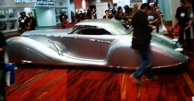A man is standing next to a silver car on a red carpet.