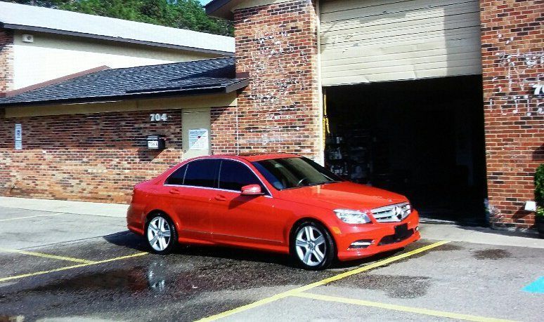A red car is parked in a parking lot in front of a brick building.