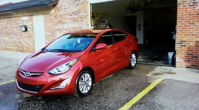 A red car is parked in a parking lot in front of a garage.