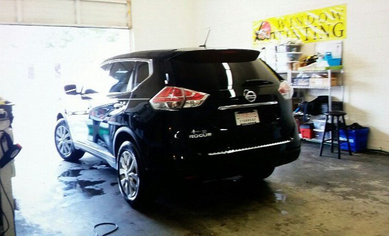 A black car is parked in a garage next to a sign that says window tinting
