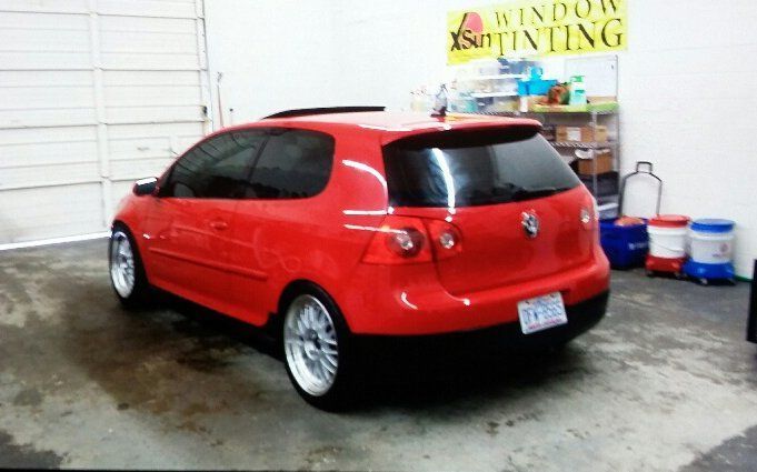 A red car is parked in front of a window tinting sign