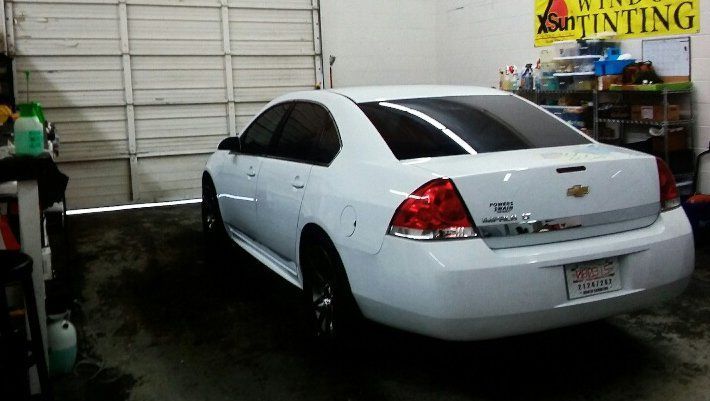 A white car is parked in a garage next to a sign that says tinting