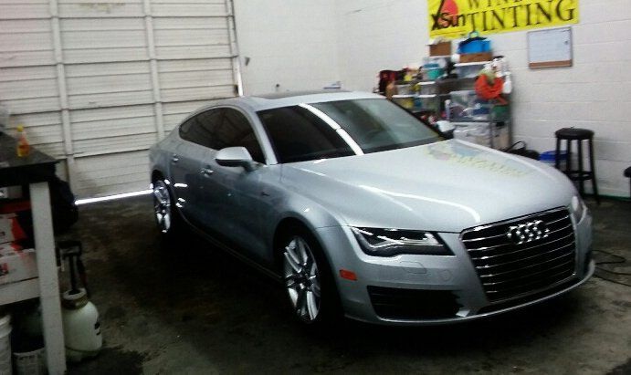 A silver audi is parked in a garage next to a sign that says window tinting