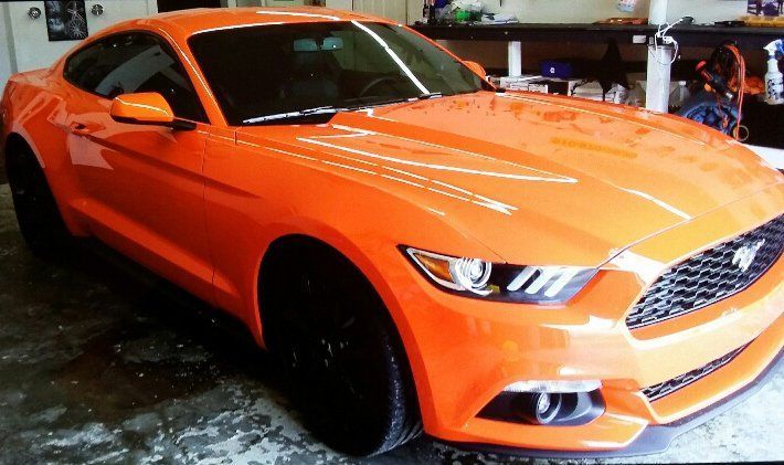 An orange ford mustang is parked in a garage.