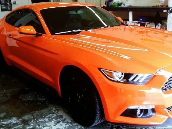 A bright orange mustang is parked in a garage