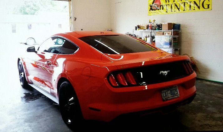 A red mustang is parked in a garage next to a sign that says tinting
