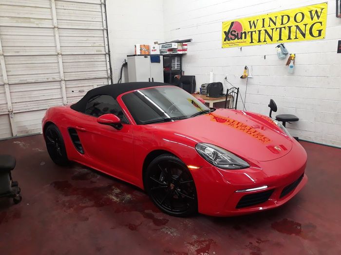 A red sports car is parked in a garage next to a sign that says window tinting