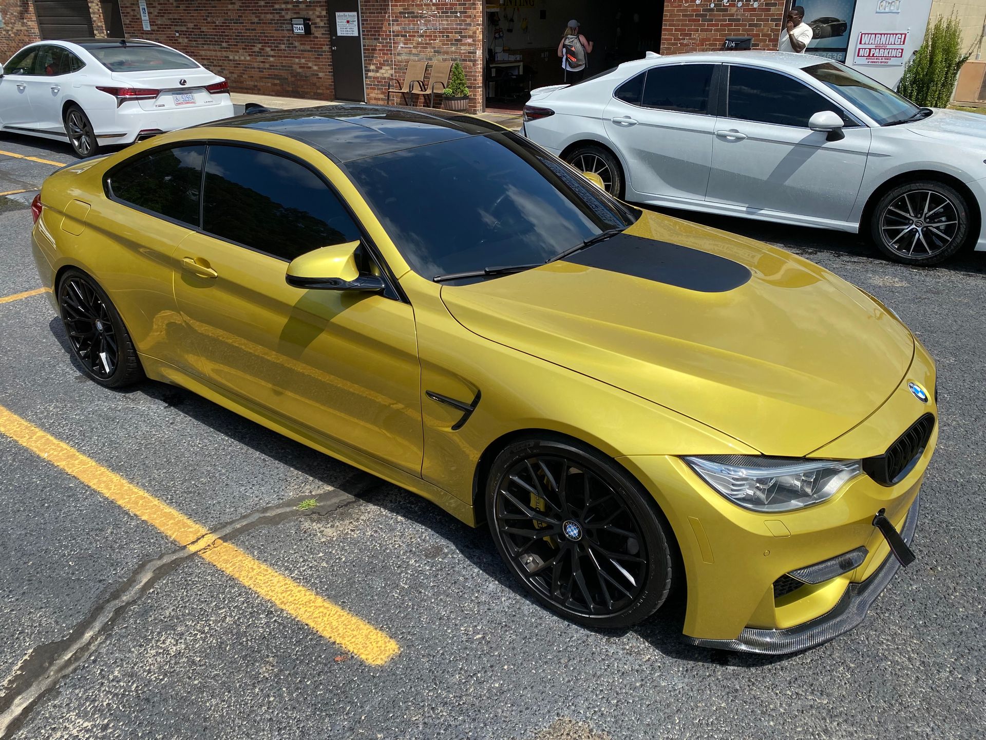 A yellow bmw m4 is parked in a parking lot next to a white car.