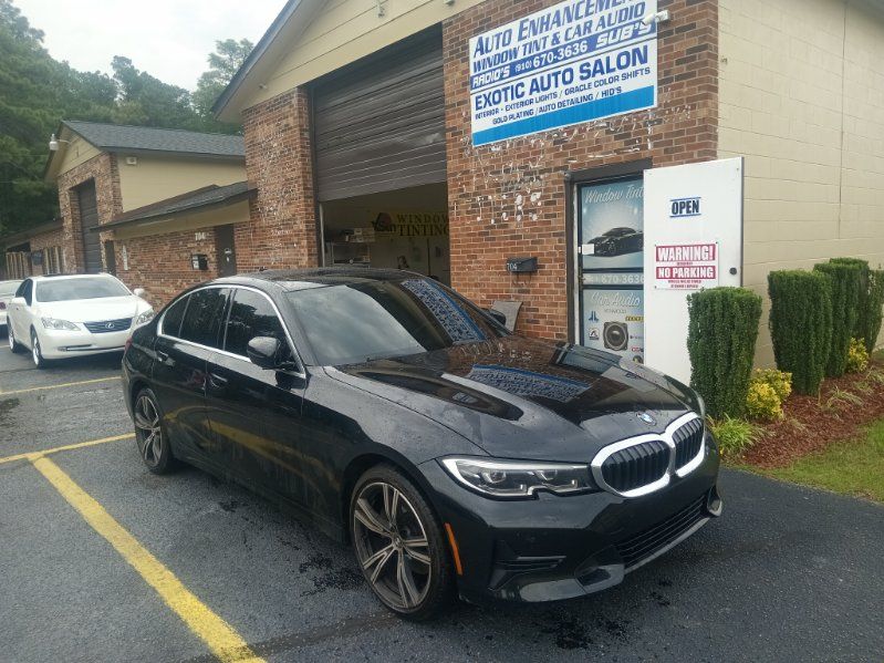A black bmw 3 series is parked in front of a brick building.