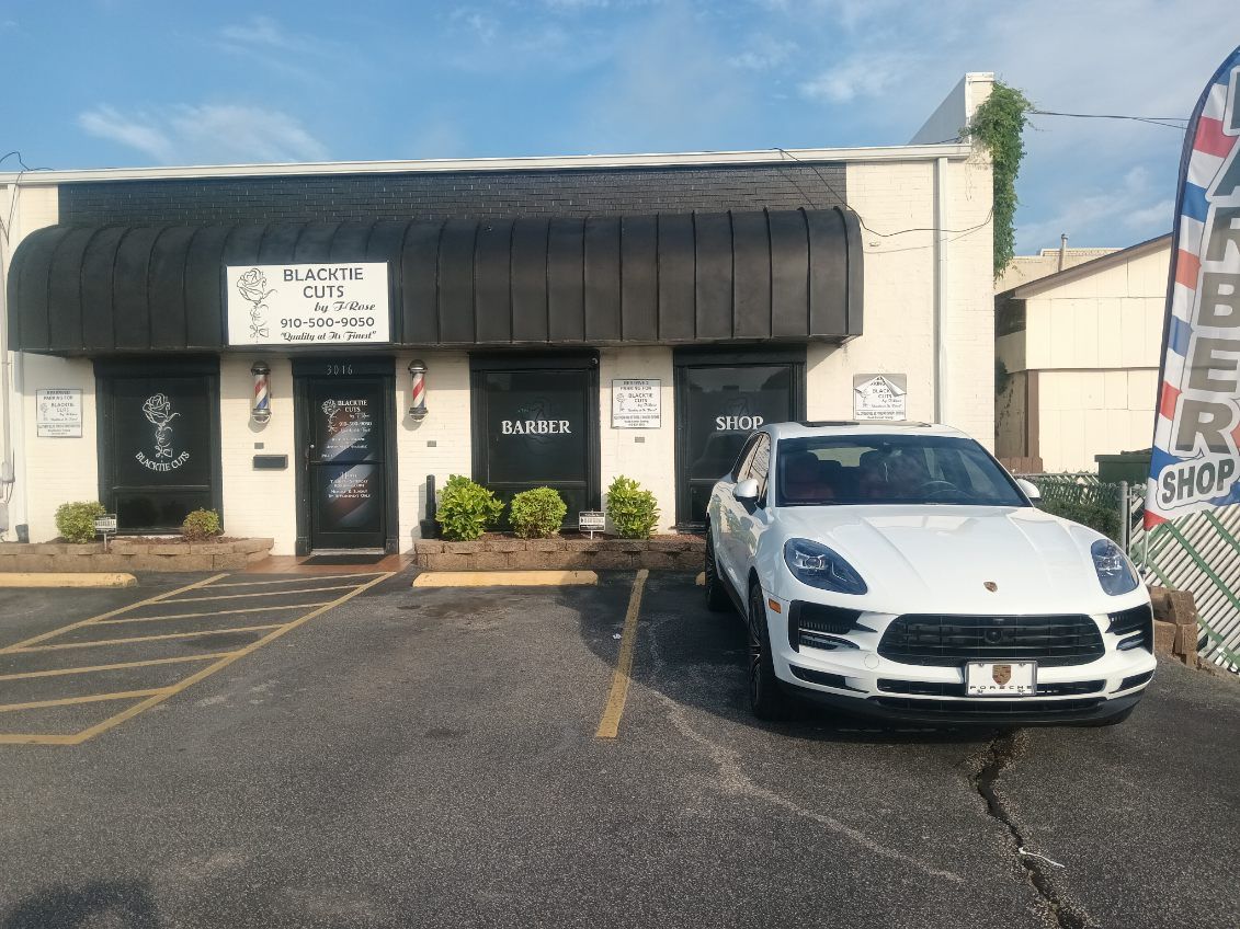 A white car is parked in front of a barber shop