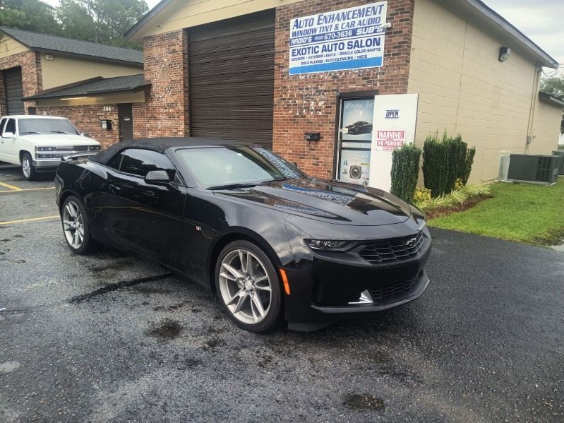A black convertible chevrolet camaro is parked in front of a building.