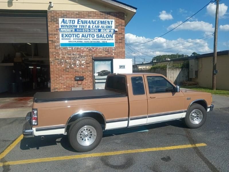 A brown truck is parked in front of a building that says auto enhancement