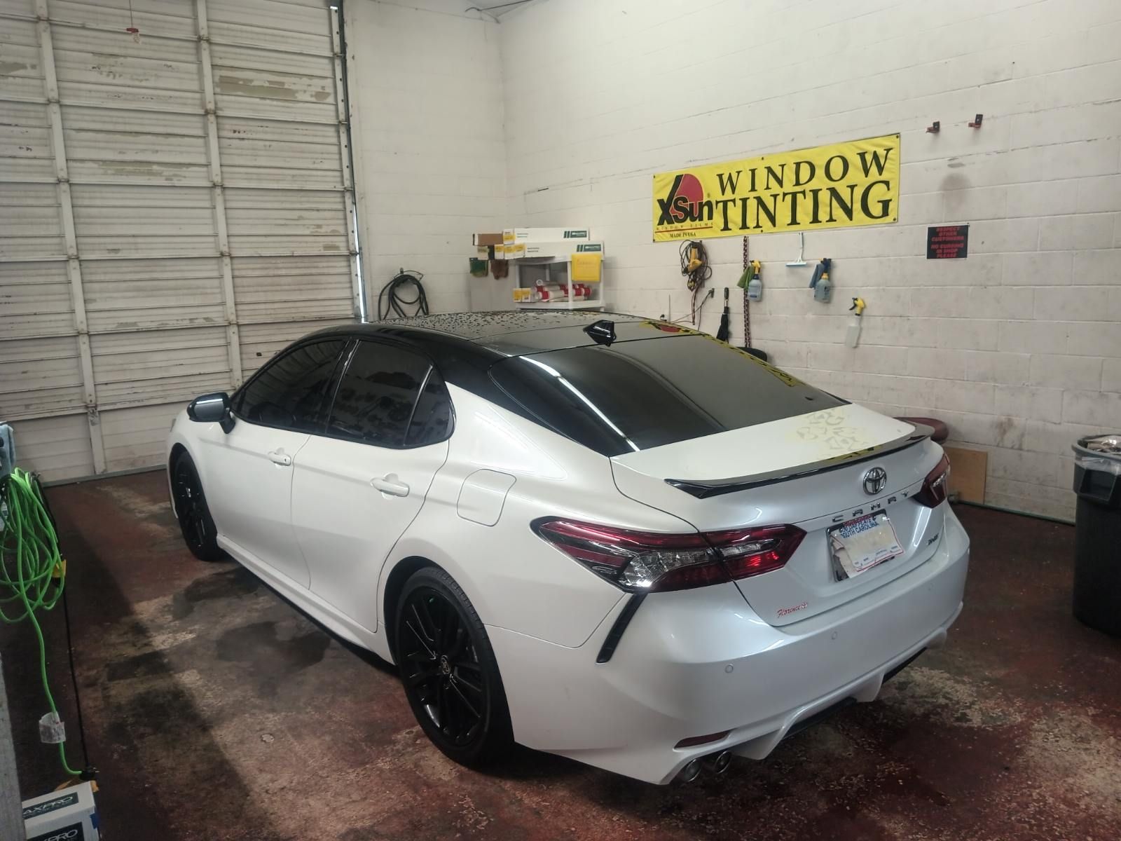 A white car is parked in a garage next to a sign that says window tinting.