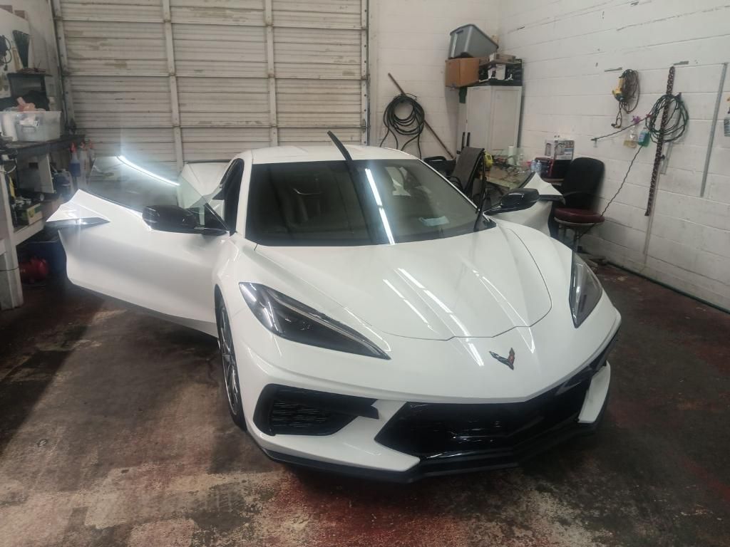 A white corvette is parked in a garage with its doors open.