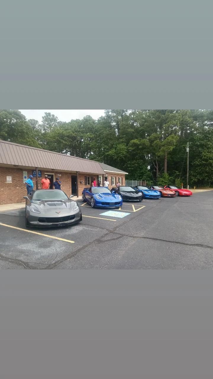 A row of cars are parked in a parking lot in front of a building.