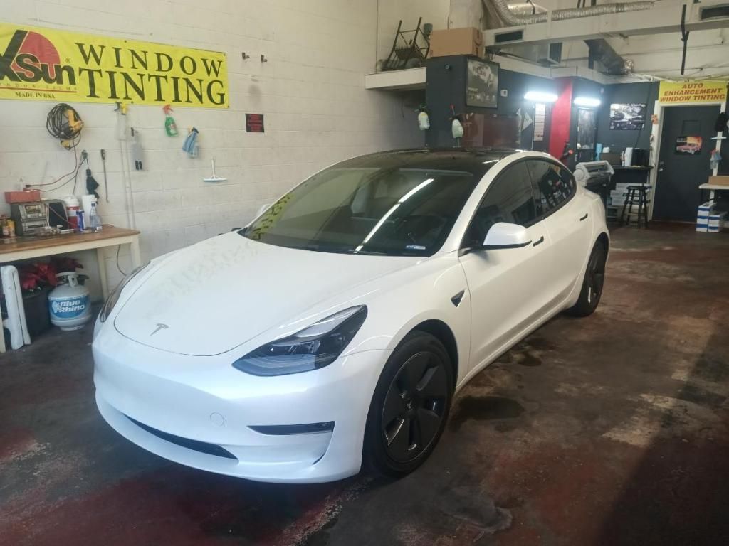 A white tesla model 3 is parked in a garage.