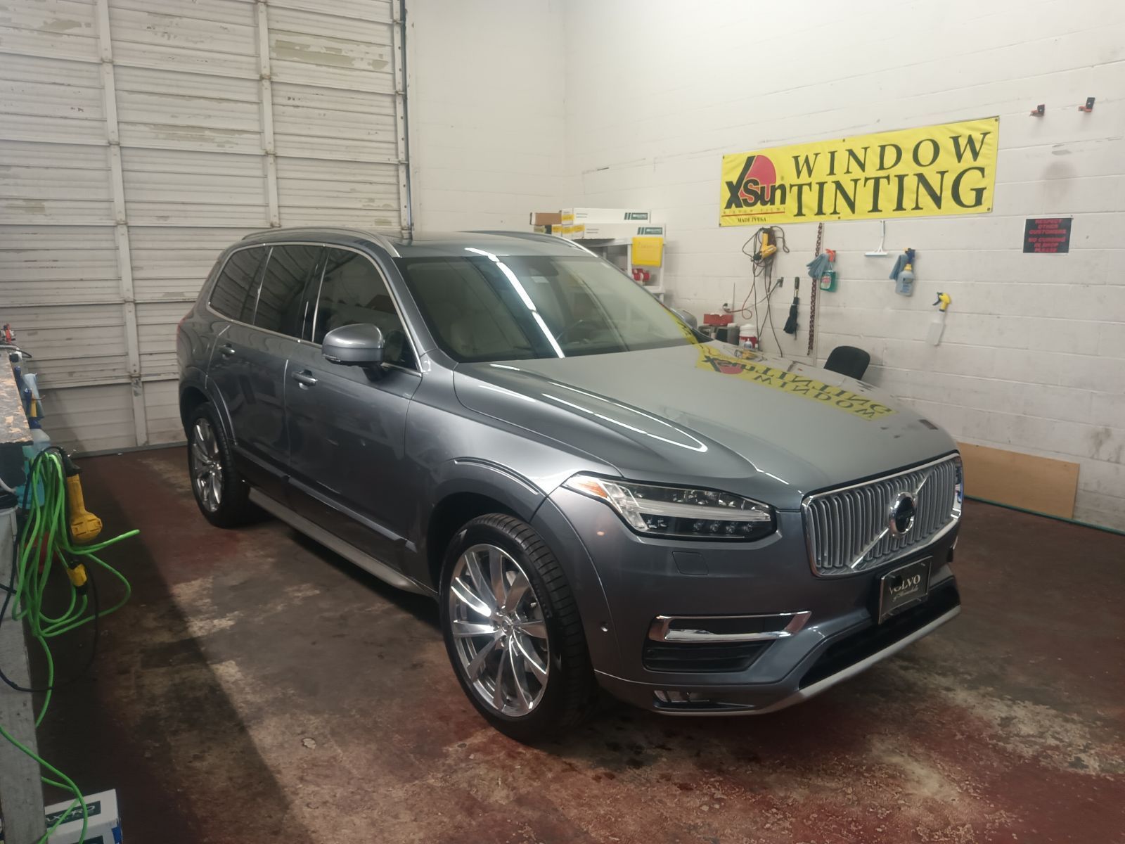 A volvo xc90 is parked in a garage next to a window tinting sign.