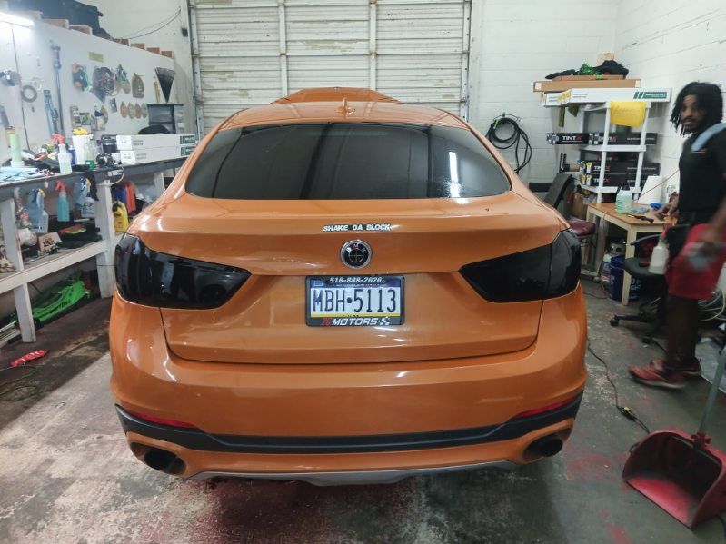 A man is standing next to an orange car in a garage.
