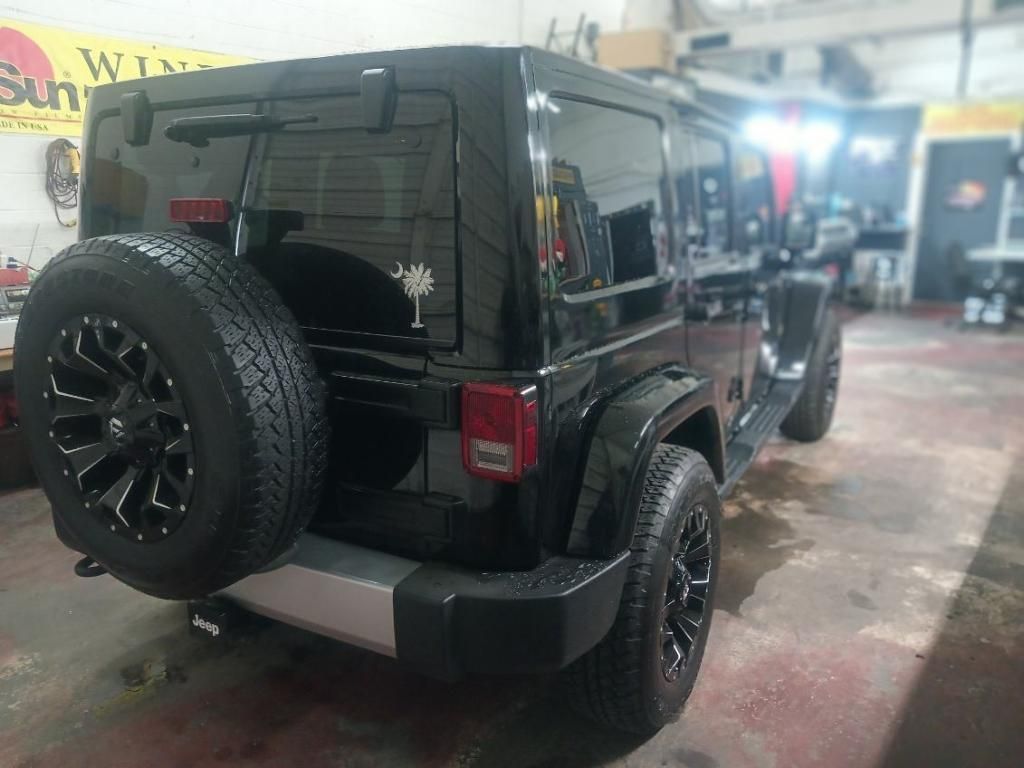 A black jeep with a spare tire is parked in a garage.