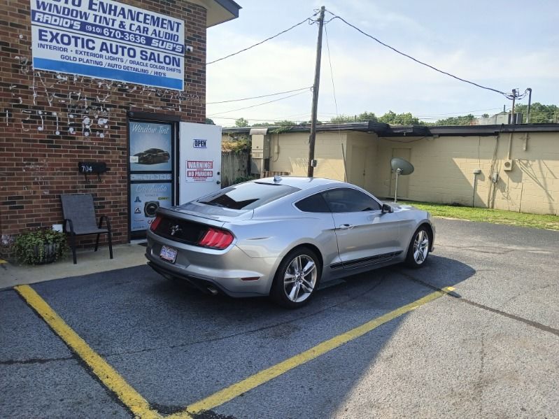A silver mustang is parked in a parking lot in front of a brick building.