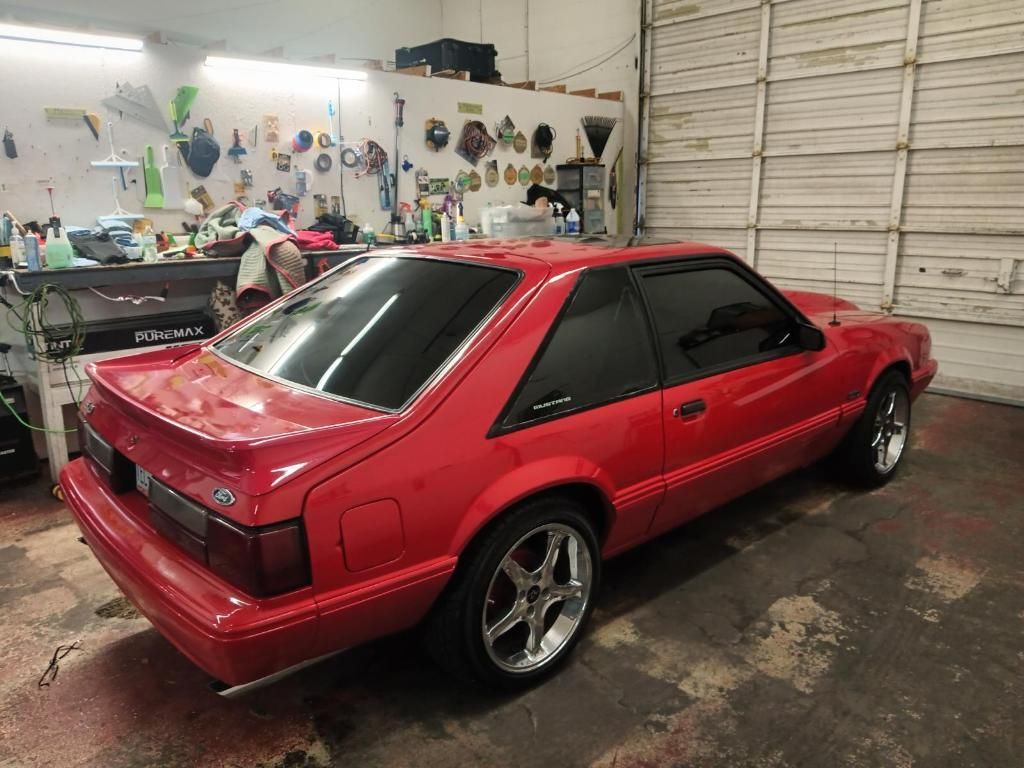 A red mustang is parked in a garage next to a garage door.