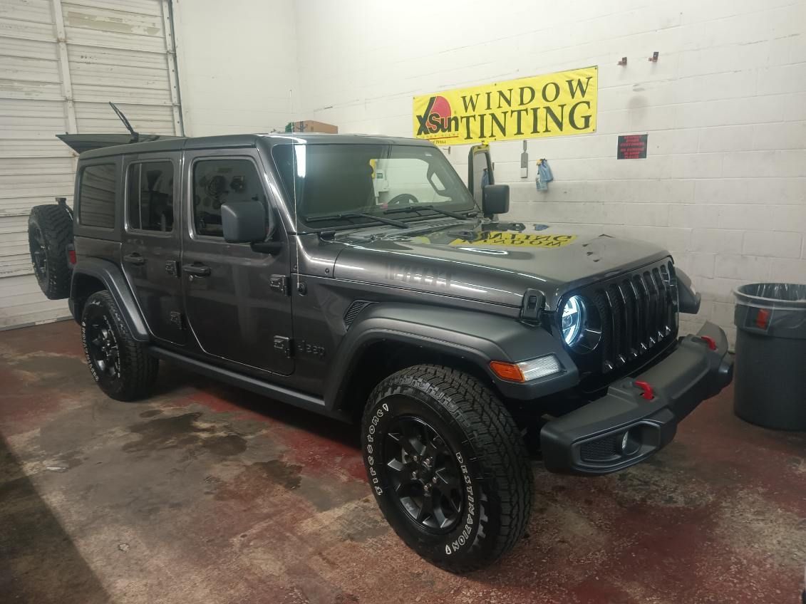 A jeep is parked in a garage next to a sign that says window tinting.